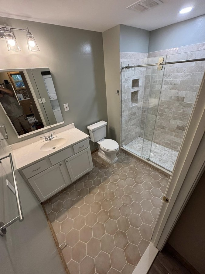 Remodeled bathroom with walk-in shower, sliding glass door, marble-look tile, and hexagon tile floor
