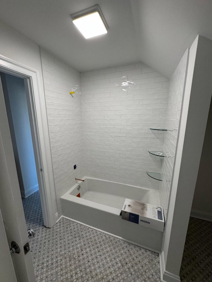 Tub and shower surround in white subway tile with glass corner shelves and mosaic tile floor
