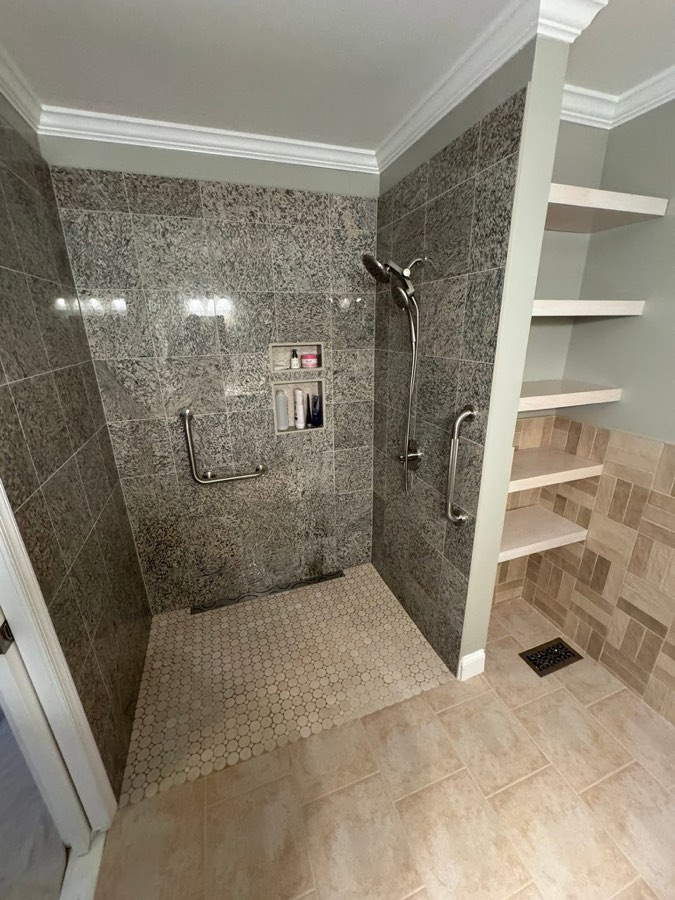 Curbless walk-in shower with granite-look tile, dual shower heads, grab bars, and built-in shelving