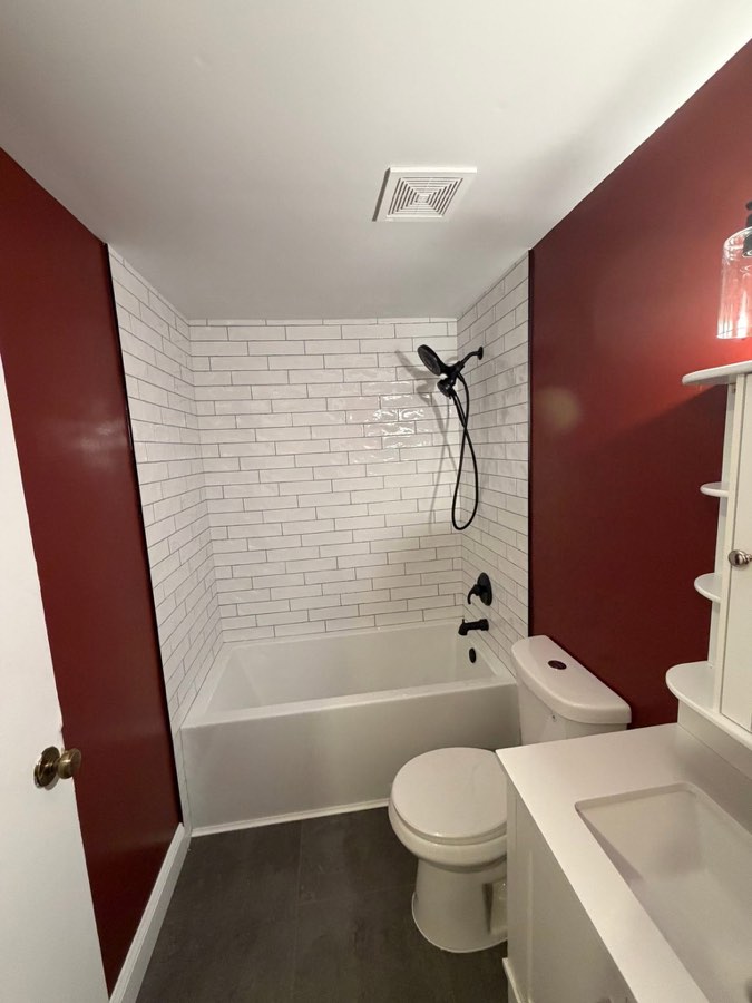 Hall bathroom with deep red walls, white subway tile tub surround, and matte black fixtures