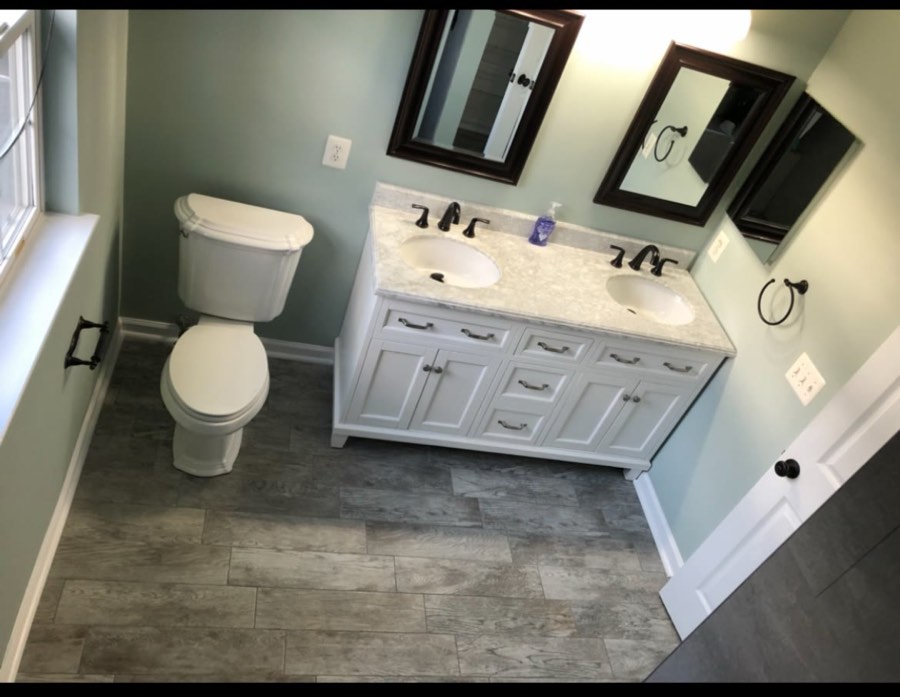 Finished primary bathroom with a double vanity, marble-look quartz top, oil-rubbed bronze fixtures and wood-look tile floor