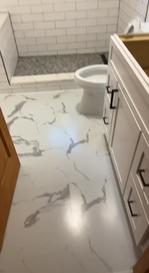 Bathroom with marble-look tile floor, white subway tile shower with hex mosaic pan, and white vanity